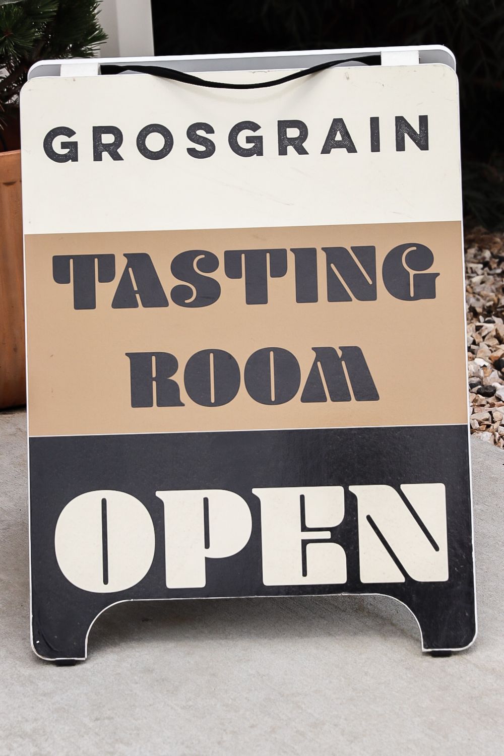 A black and tan sandwich board sign advertising 'Grosgrain Tasting Room Open' outside an establishment.