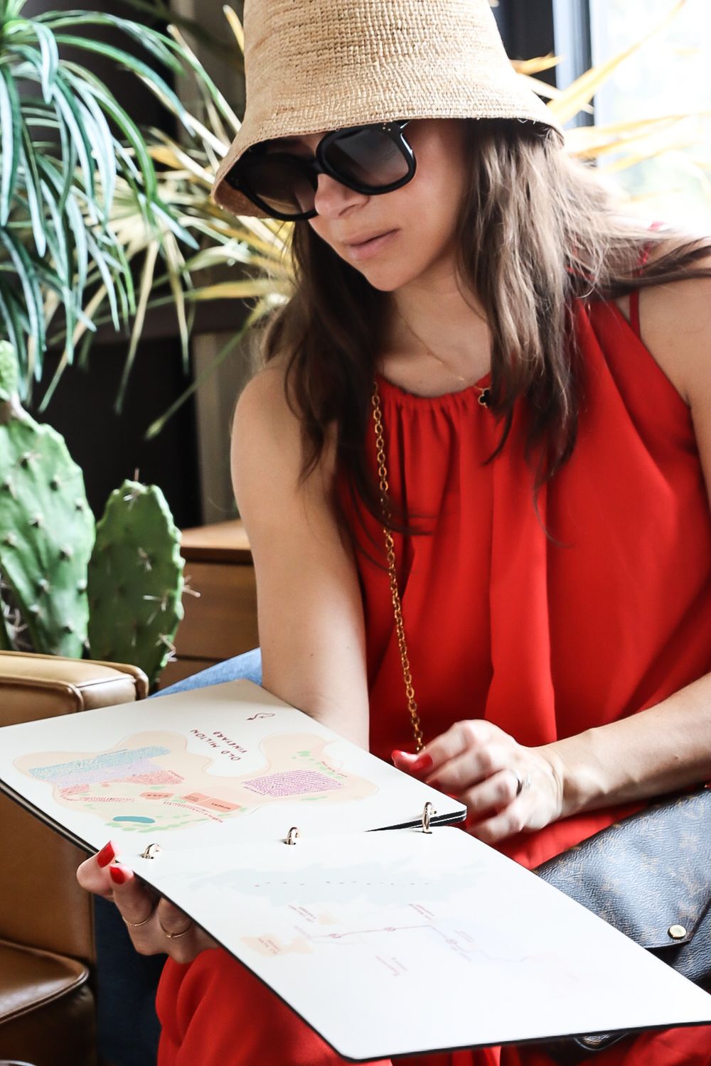 Someone in a red dress and straw hat reading a menu in a casual outdoor setting.