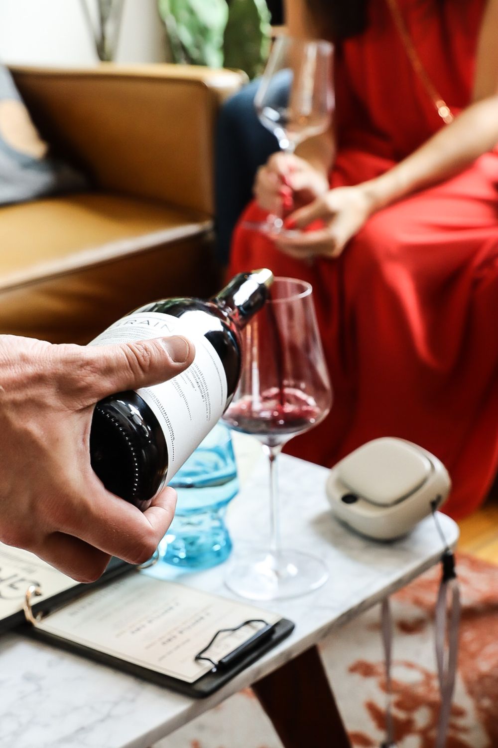 Hand pouring wine into glasses during a tasting session with menu and clipboard visible.