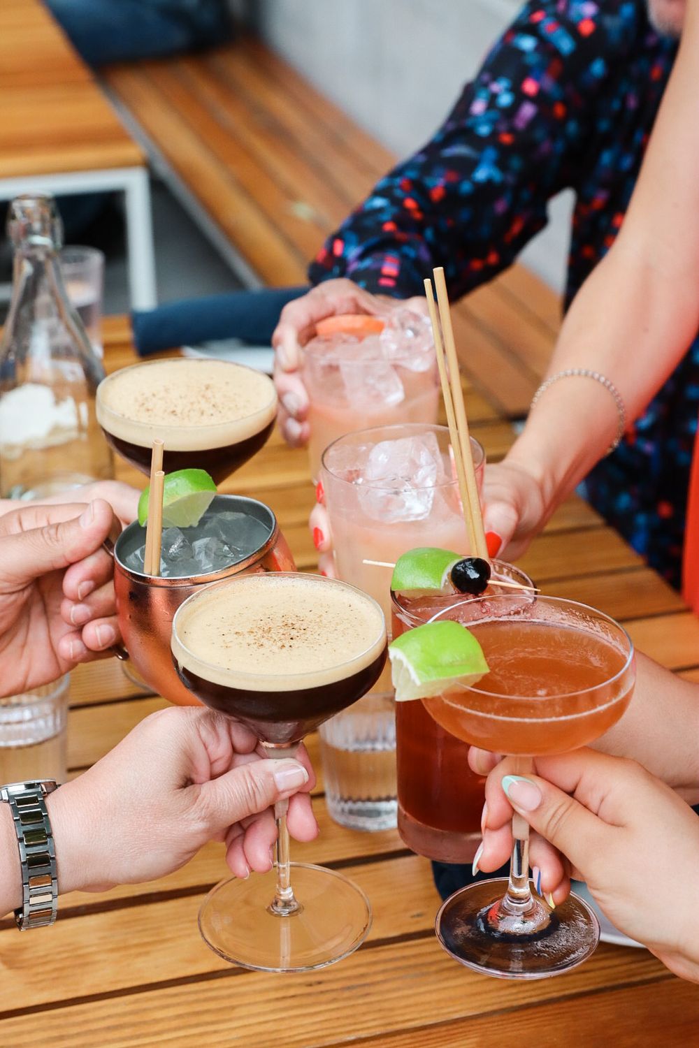 Friends toasting with colorful cocktails at a wooden table during a social gathering.
