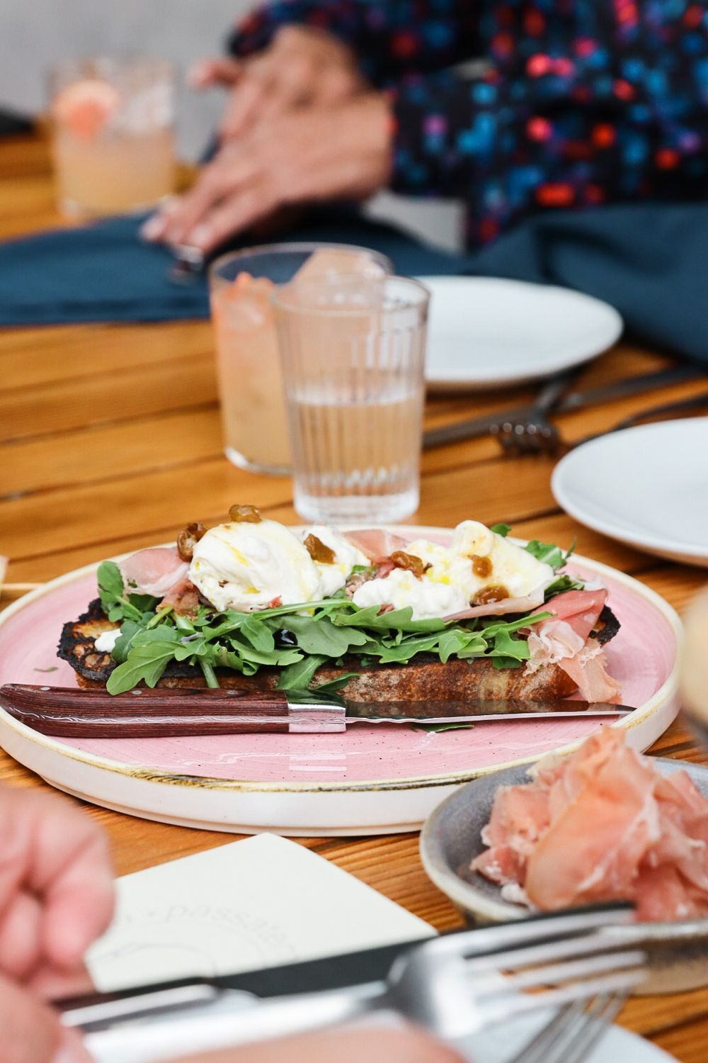 Fresh salad with burrata cheese and prosciutto served on a pink plate at wooden table.