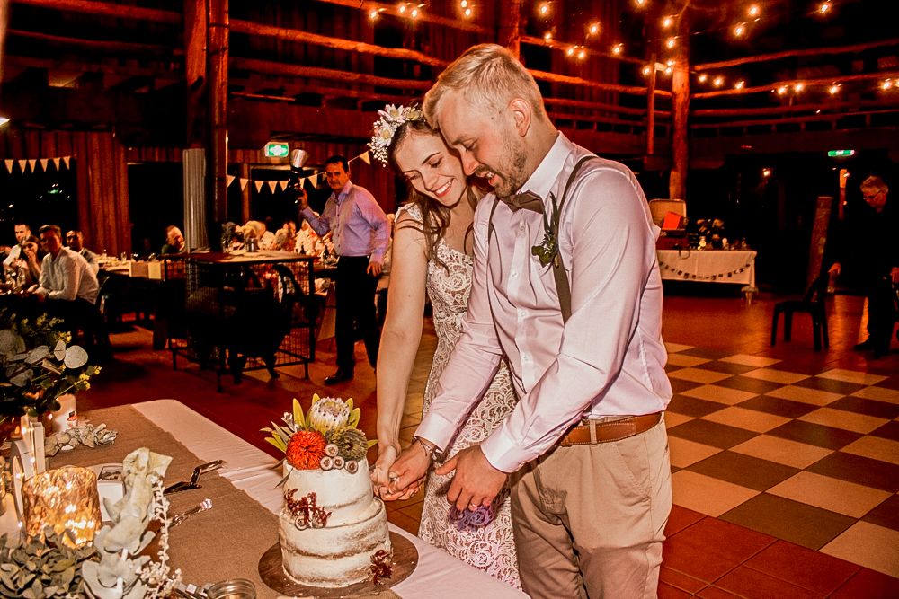 Couple cutting their wedding cake together in rustic venue with checkered floor. Nanga Bush Camp Perth Western Australia.