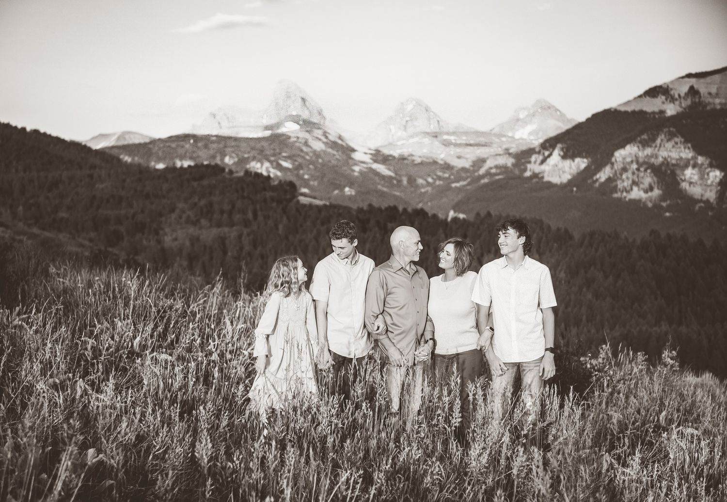 A group stands together in black and white silhouette facing mountain peaks across a wild grass meadow.