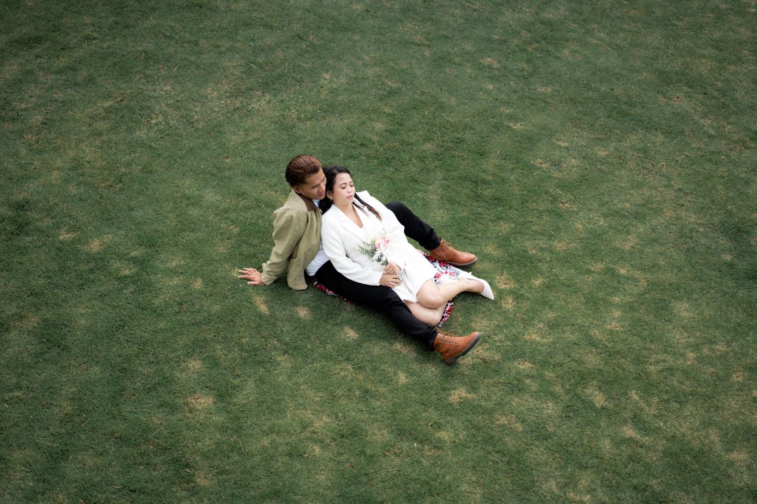 Wedding couple playfully rolling on grass in formal attire.