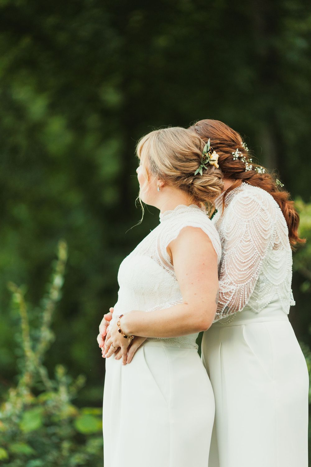Wedding party wearing white dresses standing together in an embrace.