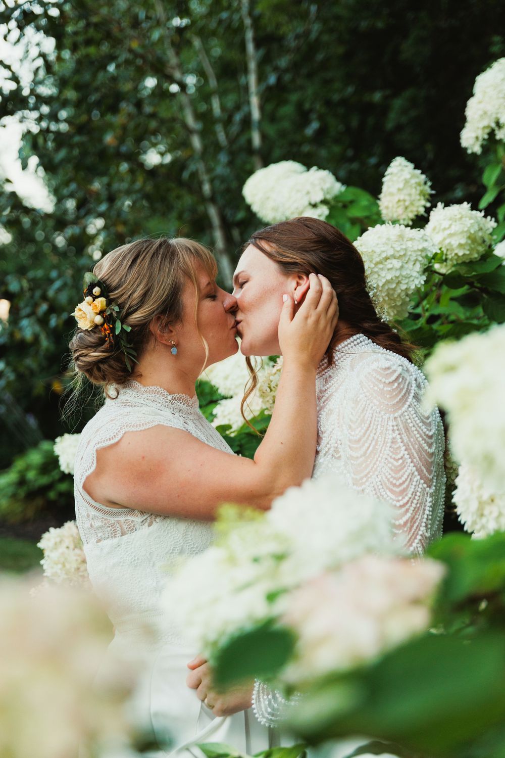 Romantic wedding kiss framed by white hydrangea flowers in a garden setting.