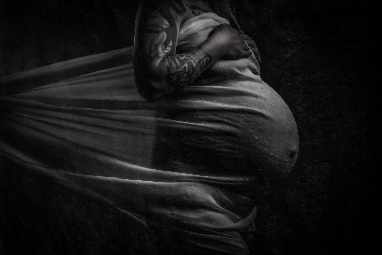 High contrast black and white pregnancy photo with billowing fabric creating dramatic silhouette.