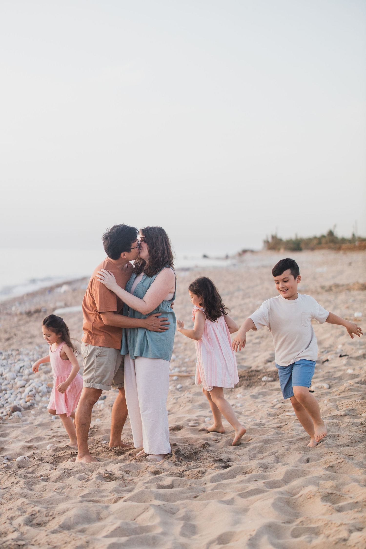 A family enjoys a playful moment together on a sandy beach during golden hour.