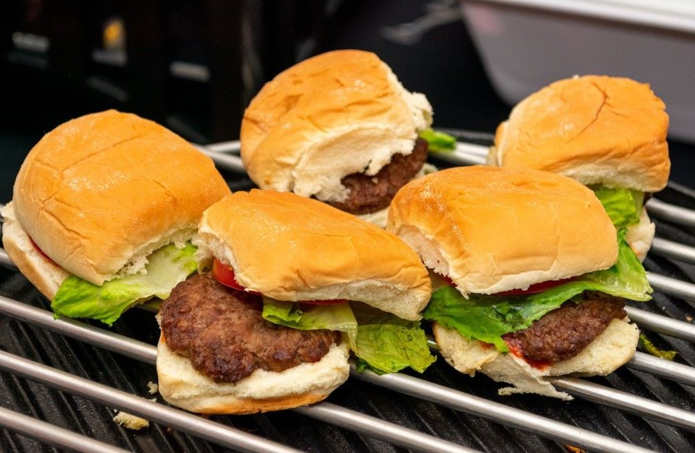 Juicy beef sliders with lettuce on golden brioche buns lined up on a black grill grate.
