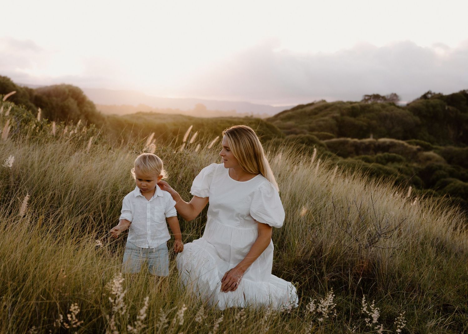 Pregnant mum and toddler at sunset on Bombo Headland, admiring wildflowers – Maternity photography in Wollongong by Lovers and Bubs.