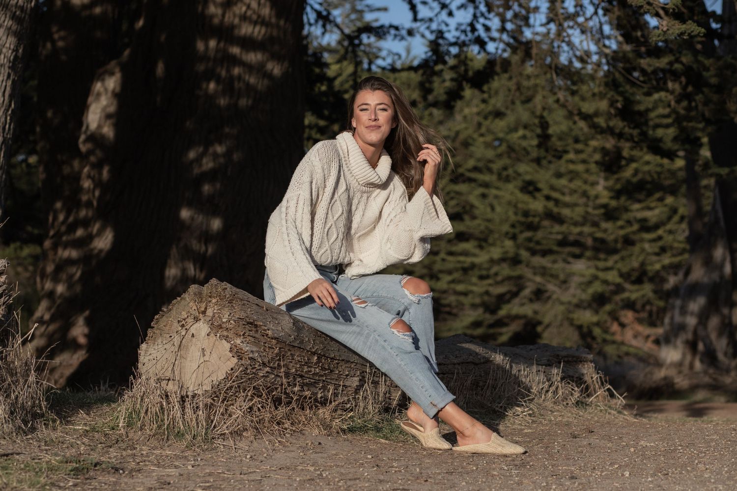 Woman in chunky knit sweater sitting on dead tree log in the park on Maui