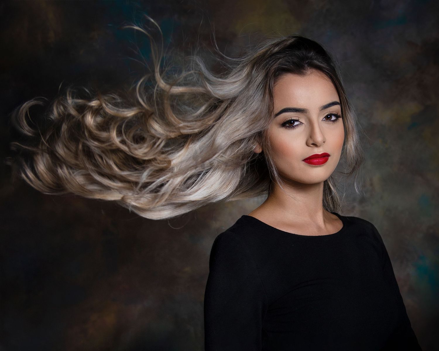 Dramatic portrait featuring flowing silver-grey hair and a black top against a dark atmospheric background.