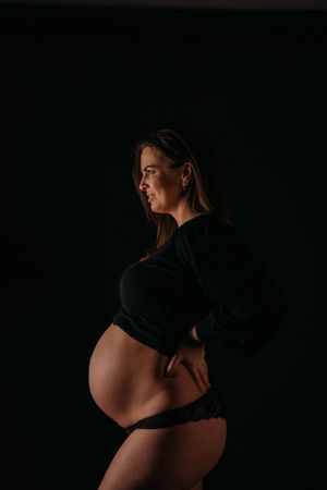 Een zwangerschapsfoto met silhouet toont een aanstaande moeder in profiel tegen een donkere achtergrond, gekleed in een zwart topje.