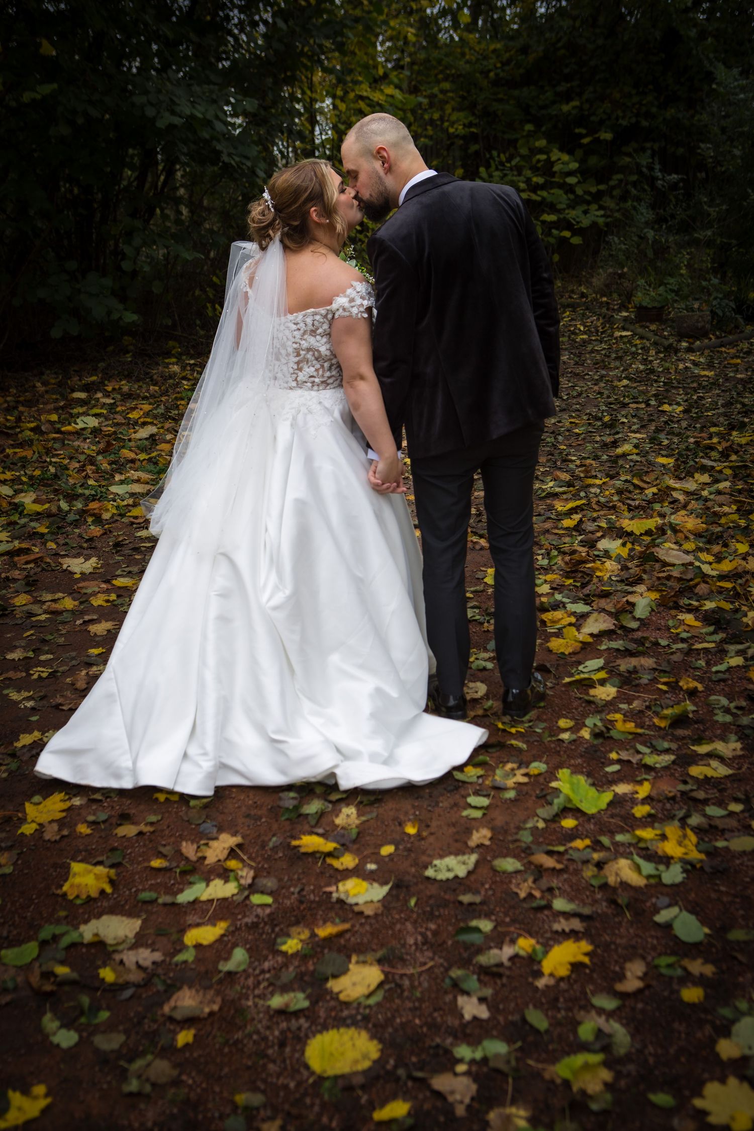 A romantic wedding portrait of a couple standing on fallen autumn leaves in a wooded area.