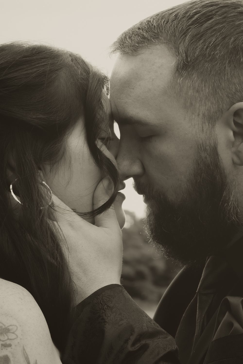 Intimate black and white close-up of a bearded man tenderly holding a woman's face as they touch foreheads.
