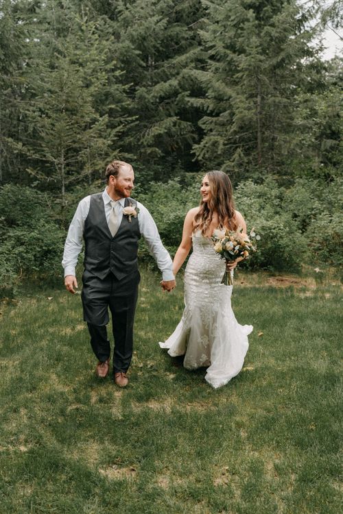 A joyful couple walks hand in hand through a woodland area during their wedding photoshoot.