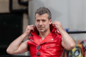 Person adjusts red leather jacket collar while standing outdoors.