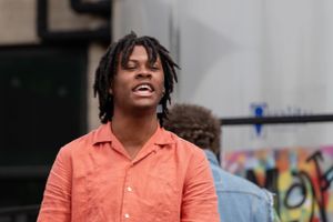 A person in a coral colored shirt smiles during an outdoor performance.