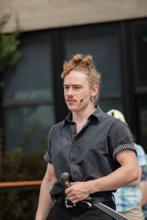 Portrait of someone with curly hair wearing a dark striped shirt and holding equipment outdoors.