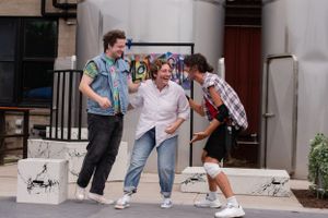 Three students playfully interacting and laughing on outdoor steps near building entrance.