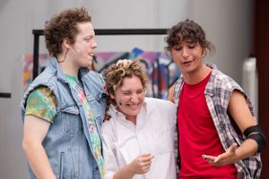 Three people stand outdoors together laughing and chatting while wearing casual summer clothing.