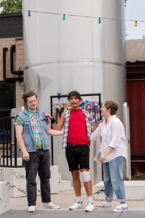 Three people stand together casually chatting outdoors beneath colorful string lights.