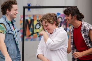 Three people sharing a lighthearted moment together in front of a colorful graffiti wall.