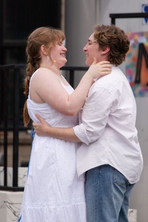 A couple embraces and smiles at each other while wearing white clothing outdoors.