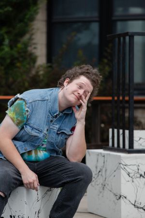 Person in denim vest sitting and laughing while resting on outdoor concrete ledge.