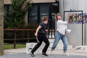 Two people in casual clothing performing dynamic movements in front of a building.