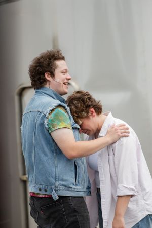 Two people share a lighthearted moment together, one wearing a denim jacket and embracing the other.