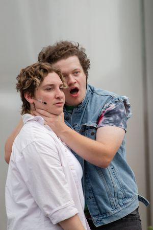 Two performers act out an intense dramatic scene while wearing casual clothing on stage.