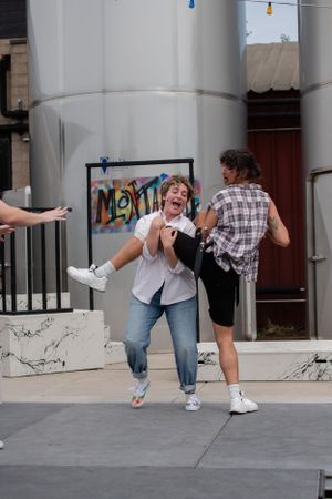 Two people share a playful moment dancing and laughing on a city sidewalk in front of a graffiti wall.