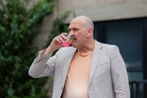 Person in light gray blazer and peach shirt taking a drink from a red cup outdoors.
