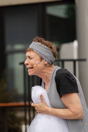 A performer in a striped headband and black shirt expresses emotion during an outdoor scene.
