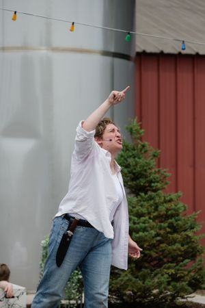 A person in a white shirt and jeans points upward while performing outdoors.