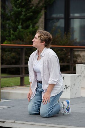 A performer kneels on a stage platform during an outdoor theatrical performance.