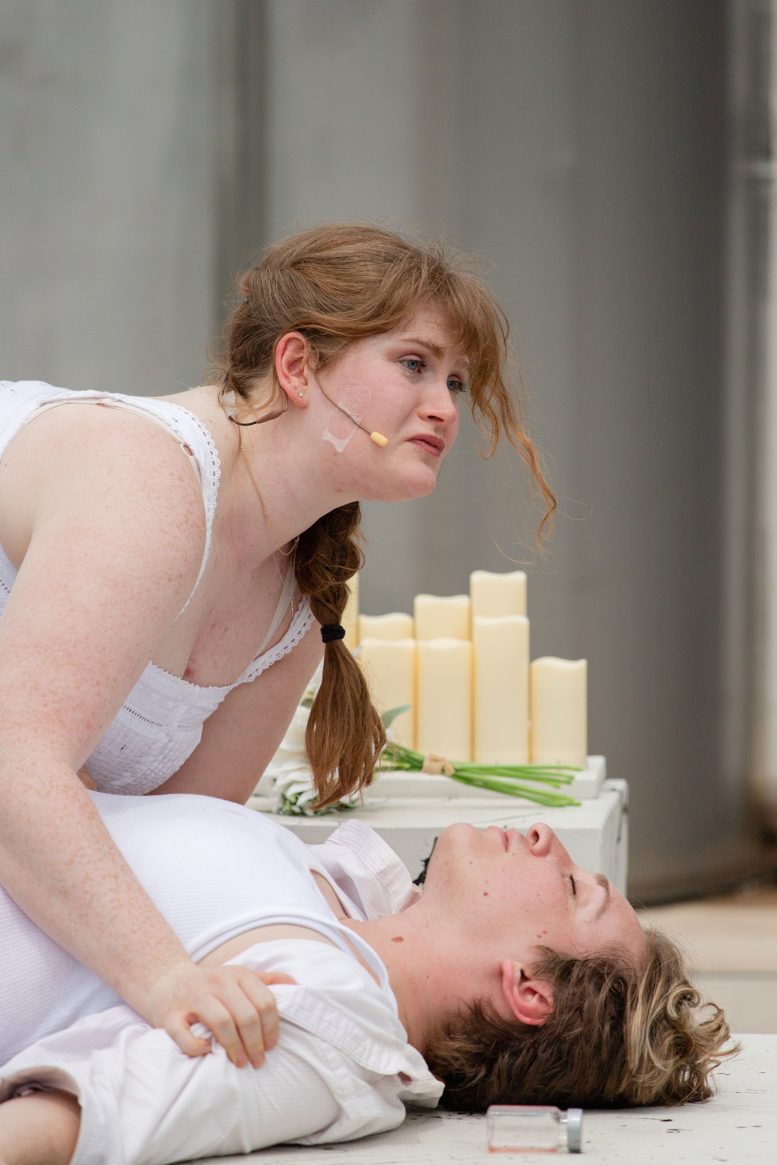 Two performers enact a dramatic scene with candles in the background during a stage production.