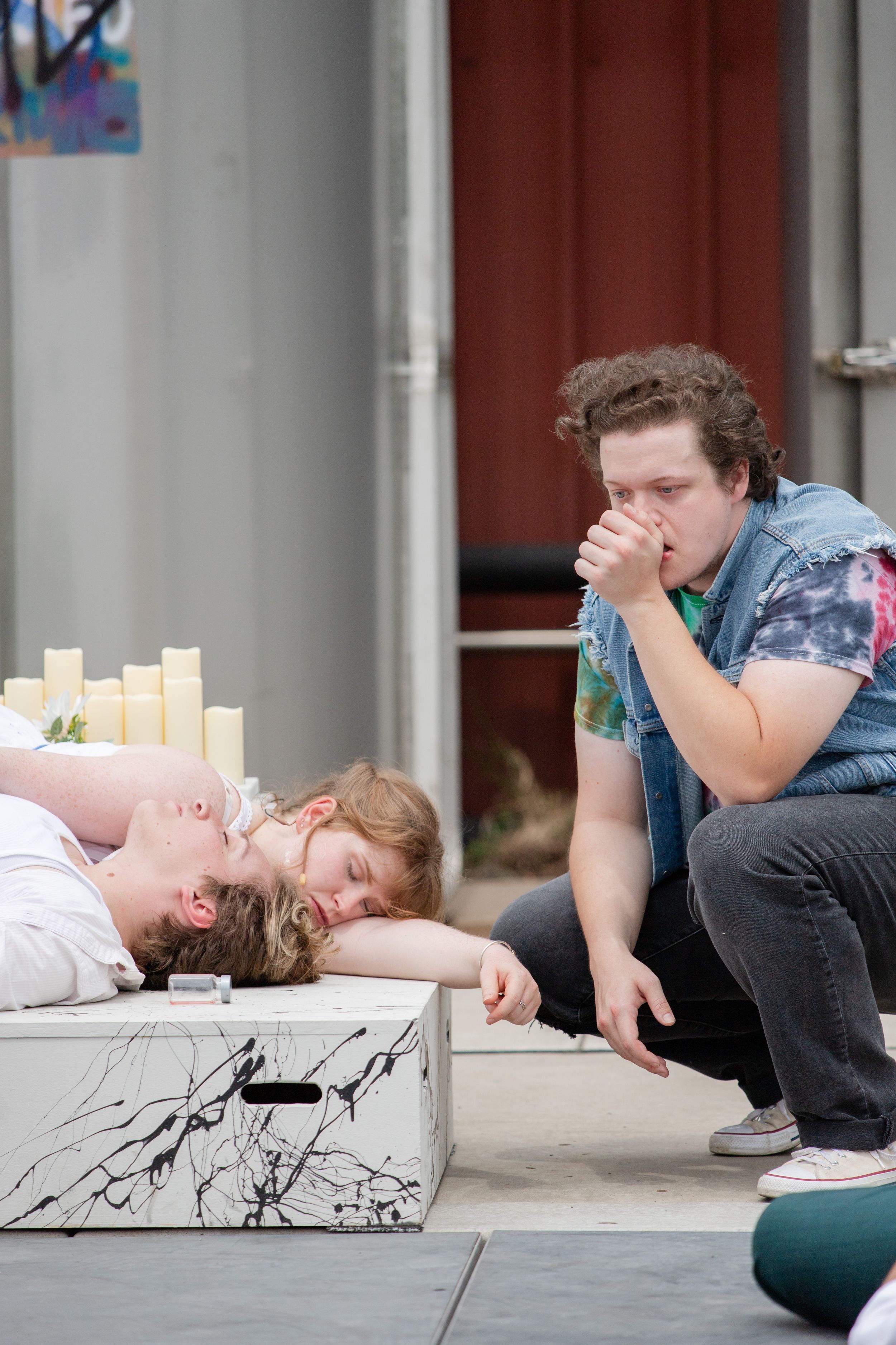 Two performers engage in an emotional dramatic scene on an outdoor stage area.
