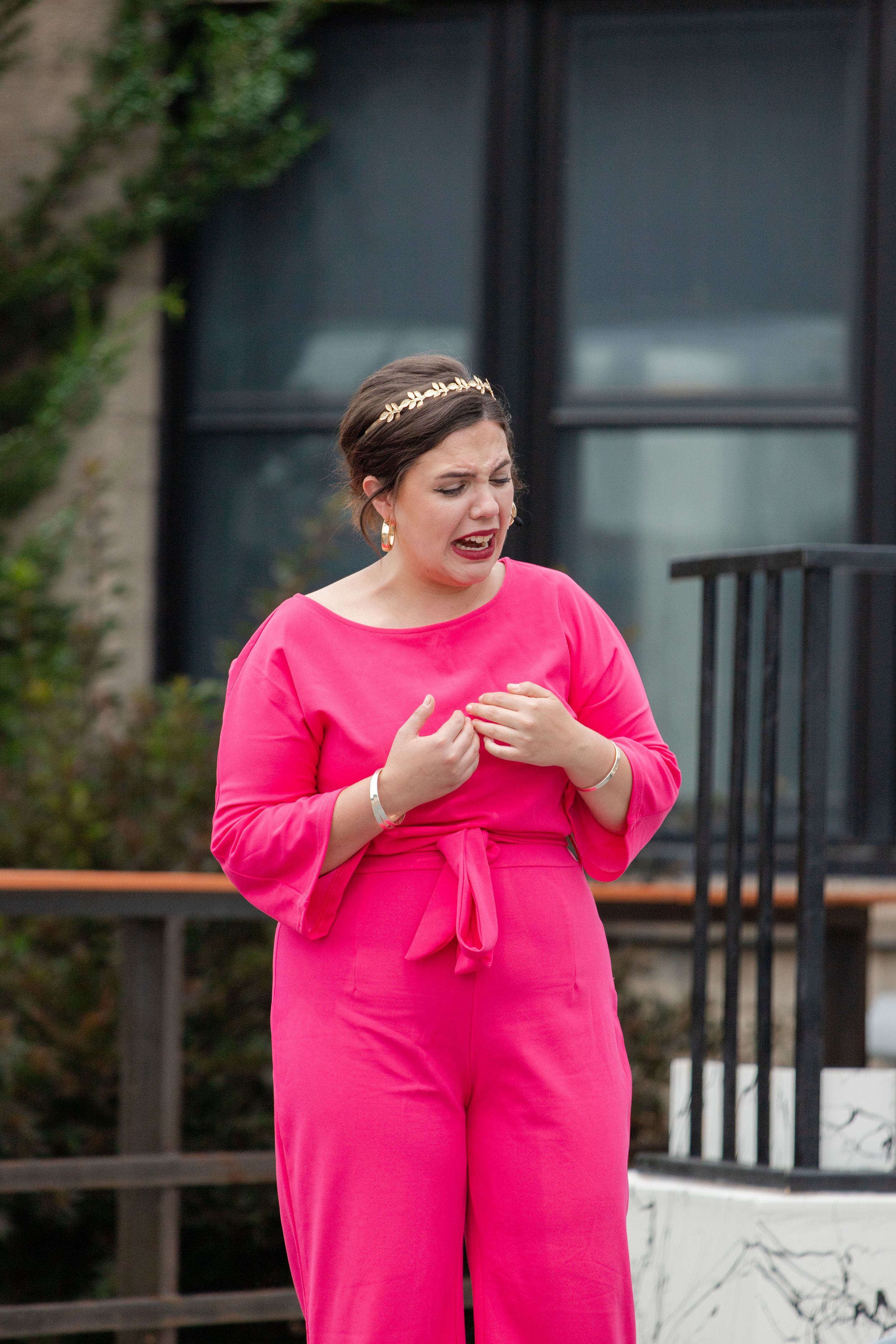 A candid style image showing someone in a vibrant hot pink jumpsuit and delicate headpiece standing outdoors.
