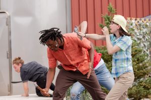 Group of people engaged in dynamic dance moves outdoors near coral colored wall.