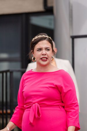 Woman wearing bright pink dress with tiara and hoop earrings poses confidently outdoors.