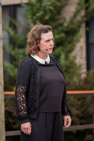 Person in black lace cardigan and dark dress standing outdoors near greenery.