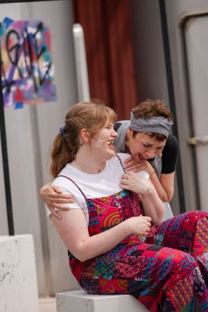 Two people sitting close together outdoors, one wearing a colorful patterned dress.
