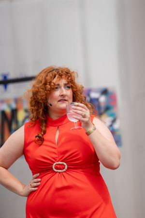Woman in red dress strikes confident pose while holding wine glass against colorful wall.