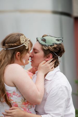 A romantic couple shares a tender kiss while wearing whimsical headpieces outdoors.