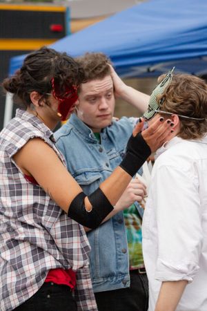 Three performers interact dramatically while wearing stage makeup and costumes.