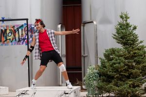 Person in red shirt and shorts leaping energetically in front of a wall with graffiti.
