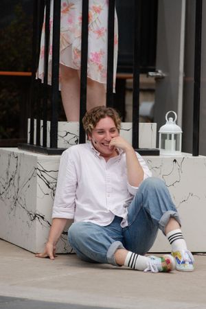 A person in a white button down shirt and jeans sits casually on a porch with decorative lanterns.