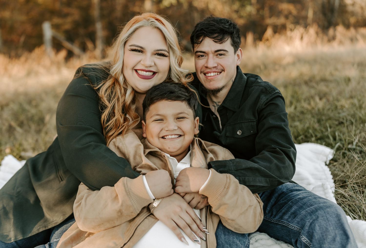 A loving family portrait taken outdoors in autumn with warm golden lighting and natural expressions.